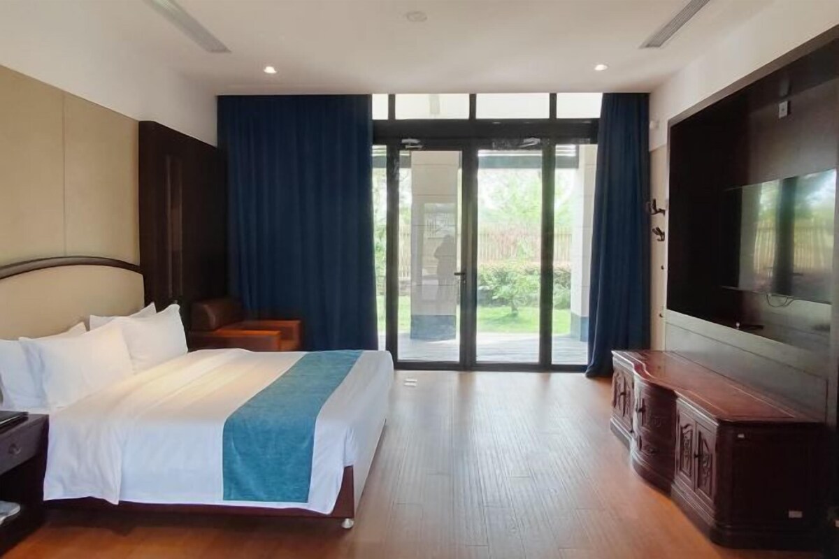 A hotel room with a bed, a TV, a desk, and a view through a glass door.