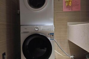 Un lave-linge à chargement frontal dans une buanderie, avec des murs carrelés et un manuel d’instructions bien visible.