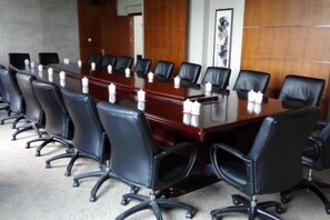 Un salón de conferencias con una larga mesa, sillas de cuero negro y un panel de pared de madera.