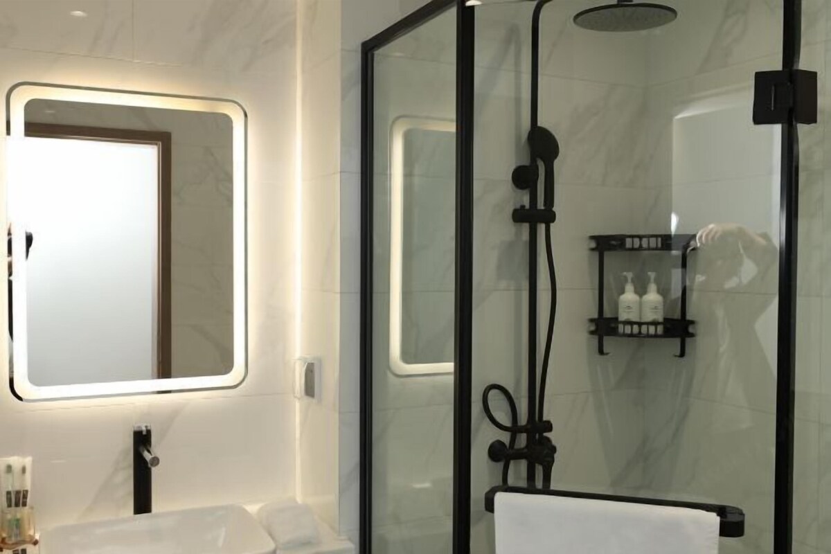 A modern bathroom with a glass-enclosed shower, a large mirror with integrated lighting, and a shelf with toiletries.