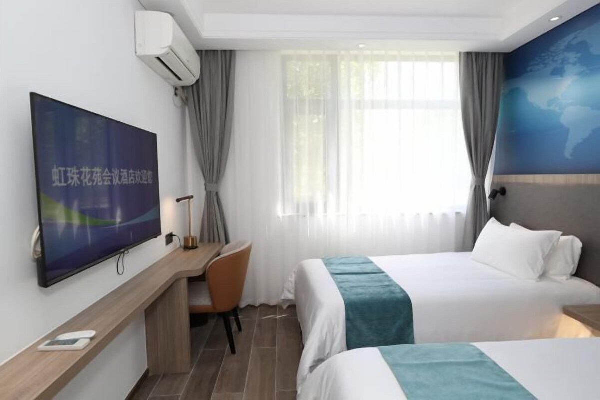 A hotel room with a bed, a desk, a chair, a TV, and a window with curtains.