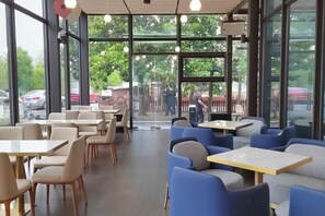 Un espacio interior con mesas y sillas, ventanas grandes y vistas al exterior.