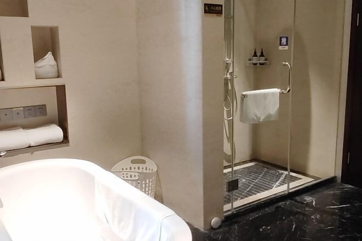 Un baño con ducha envuelta en vidrio, bañera y estante con toallas.