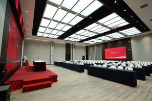 Une salle de conférence équipée d’une scène, de rangées de chaises et d’un grand écran.