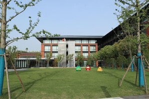 A modern building with a central glass facade, surrounded by a well-maintained lawn and trees. - Shanghai Hongzhu Garden Hotel (Shanghai)