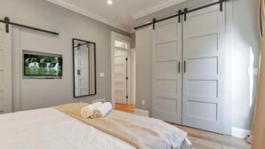 Une chambre à coucher comprenant un lit, un téléviseur, un placard à portes coulissantes et un miroir.
