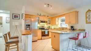 Eine moderne Küche mit Holzausstattung, Edelstahlgeräten und einer Arbeitsplatte aus Granit. Zwei Barhocker und eine kleine Kücheninsel mit Spüle sind vorhanden.