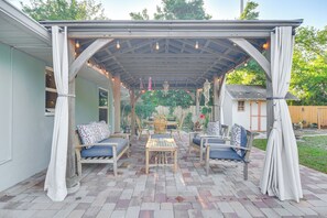 A covered patio with wooden furniture, string lights, and a view of a house in the background. - Lovely St Petersburg Home w/ Backyard Oasis (St. Petersburg)