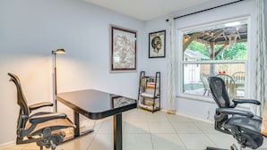Ein Zimmer mit Schreibtisch, zwei Bürostühlen, einer Stehlampe und einem Bücherregal.