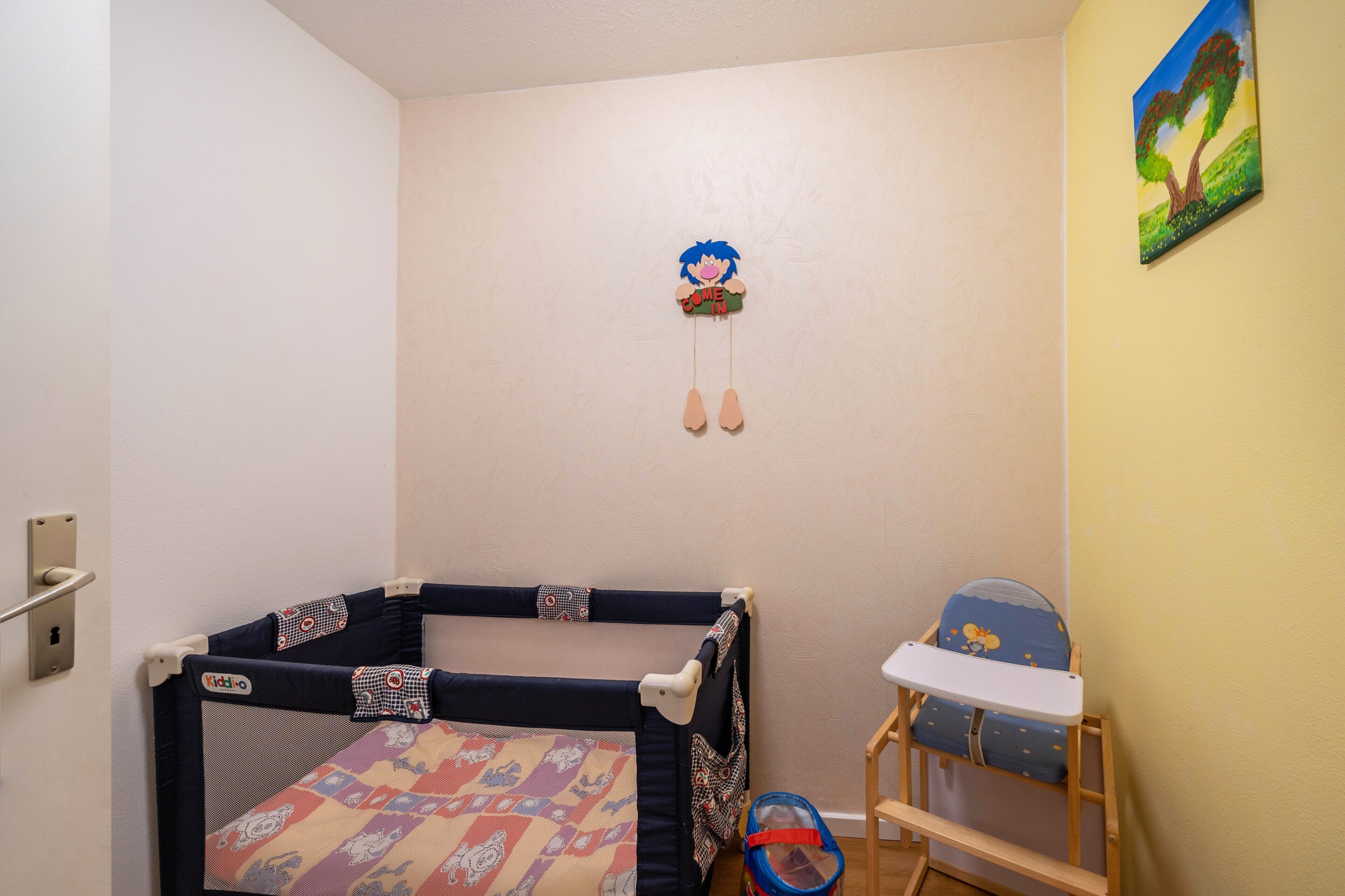 A child's play area with a cot, a high chair, and a wall-mounted decoration.