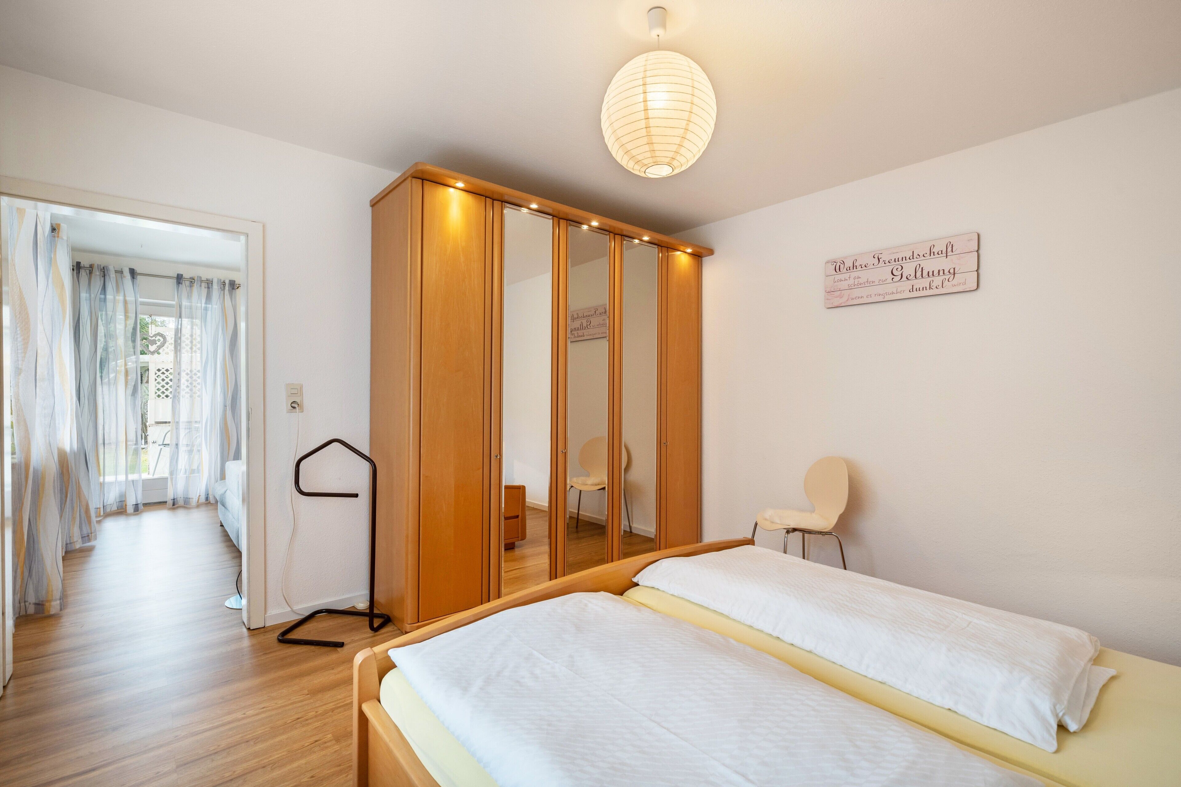 Een slaapkamer met een bed, een kledingkast, een stoel en een hanglamp.