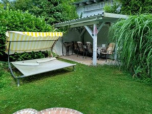 En täckt uteplats med ett bord och stolar, en liten studsmatta och en vacker trädgårdsmiljö.