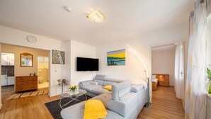 A modern living room with a grey sectional sofa, a flat-screen TV, and a painting of a landscape.