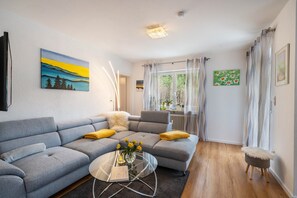 Een moderne woonkamer met een grijze modulaire bank, een glazen salontafel en uitzicht op het buitenlandse terrein door dunne gordijnen.