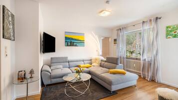 Ein Wohnzimmer mit grauem Sofa, einem Glastisch und einem Gemälde an der Wand.