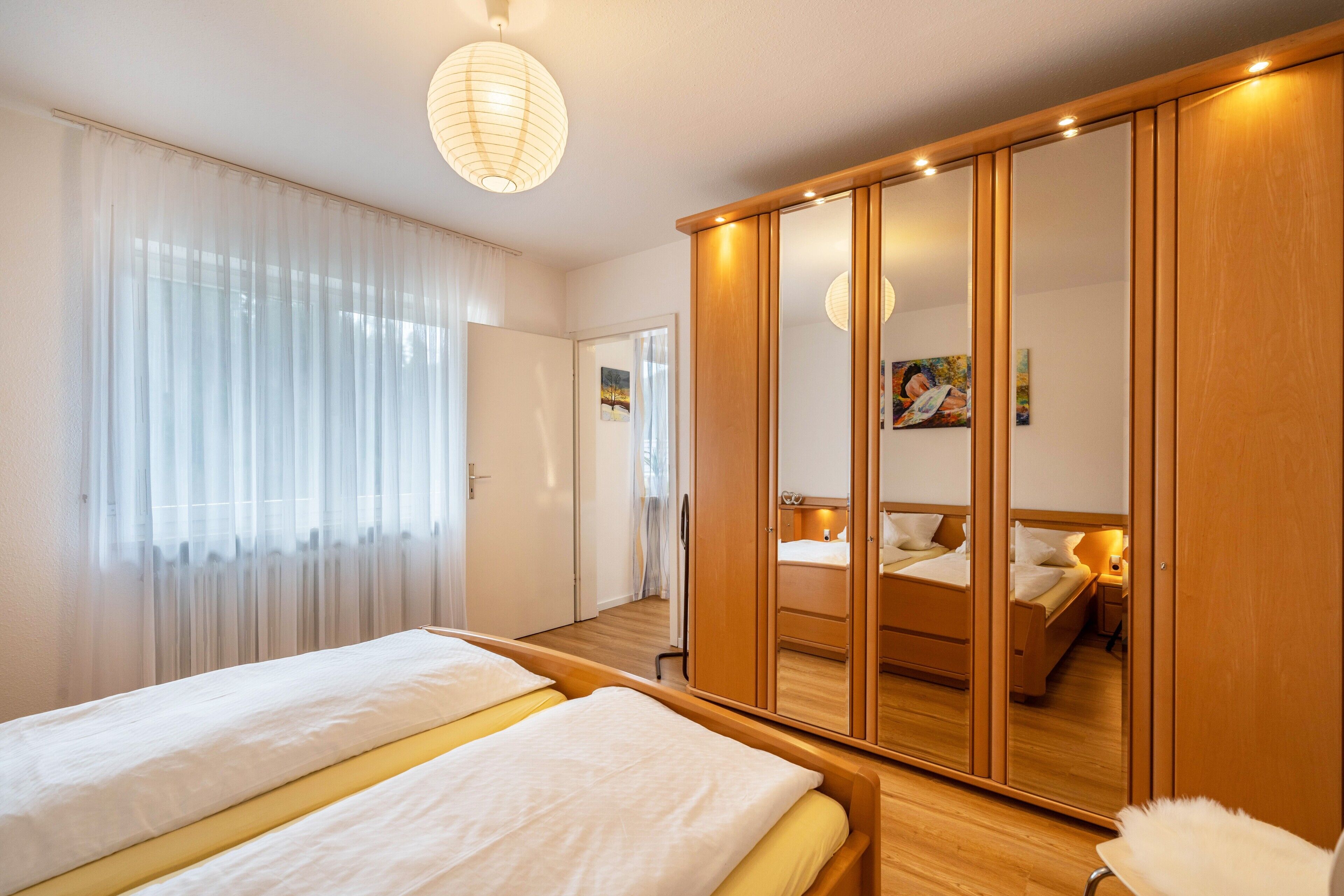 Una habitación de hotel con cama, armario, espejo y ventana con cortinas.