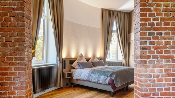 A bedroom with a brick wall, a bed with pillows, a radiator, and a window. - Apartment 'Erstes Obergeschoss' with Wi-Fi (Cuxhaven)