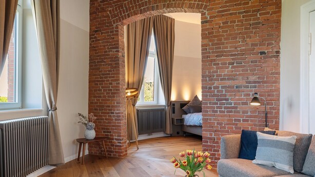 Un salon chaleureux avec un mur en briques, un canapé, un plancher en bois et un vase rempli de fleurs.