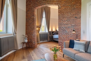 A cozy living room with a brick wall, a sofa, a wooden floor, and a vase with flowers.