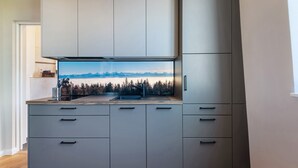 Une cuisine moderne avec des meubles gris, une cuisinière encastrée et une grande fenêtre donnant sur un paysage montagneux.