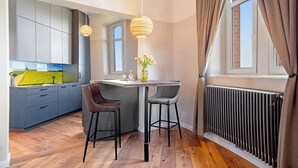 Una cocina moderna con armarios grises, piso de madera, barra con taburetes y una ventana con cortinas.