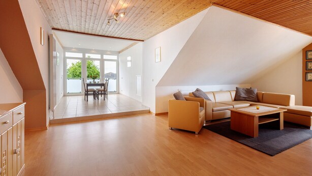 Una sala de estar moderna con techo de madera, un conjunto de sofá, una mesa de centro y vistas a través de un ventanal.