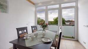 Un comedor con una mesa dispuesta para cuatro personas, un florero con flores y un balcón con vistas a casas.