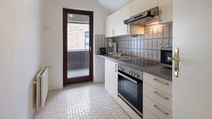 Una cocina compacta con armarios blancos, un horno negro y un respuesto de azulejos.