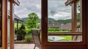 Une vue depuis une pièce dont la fenêtre donne sur un jardin, avec une table et une chaise.
