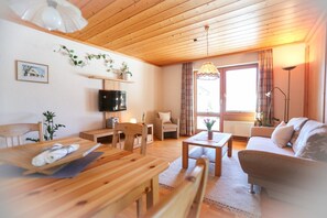 A cozy living room with wooden furniture, a flat-screen TV, and a large window with curtains.