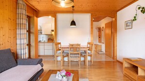 Une pièce chaleureuse avec un canapé, une table à manger et des chaises, un luminaire suspendu et, au fond, un coin cuisine.