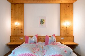 A bedroom with a wooden headboard, two bedside tables, a bed with patterned bedding, and wall-mounted lights.