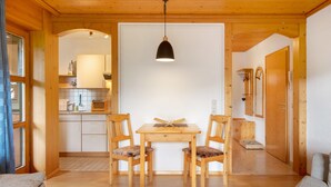 Een houten interieur met een eettafel, twee stoelen, een hanglamp en een keukenhoek.