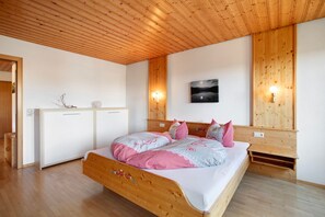A wooden ceiling, a bed with a wooden frame, a white wardrobe, and a wall-mounted picture.