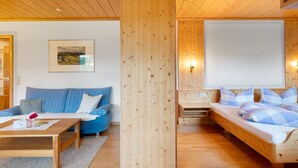 Een kamer met houten lambrisering, een bank, een bed, een tafel en een lijst met een afbeelding aan de muur.