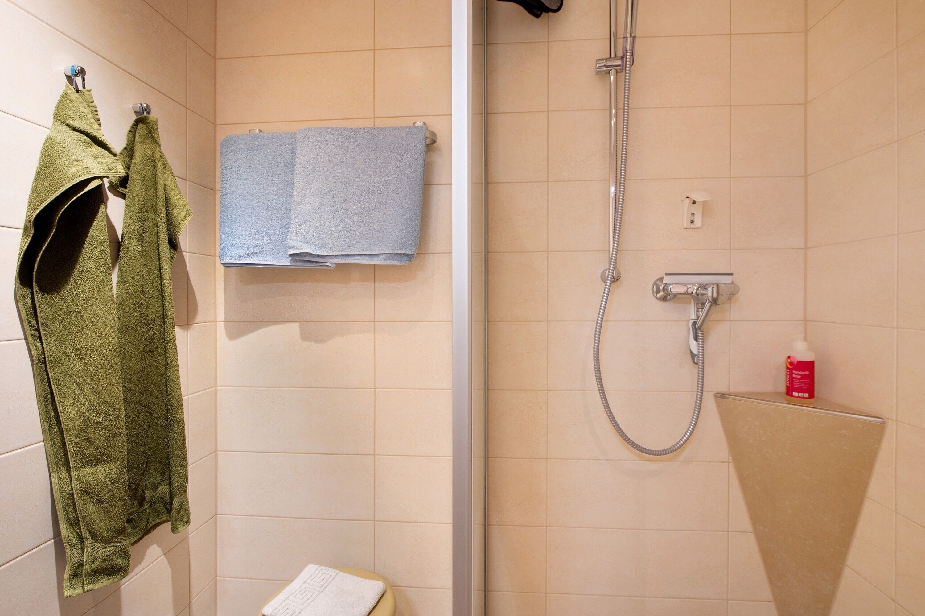 A bathroom with a shower, two towels, and a soap dispenser.