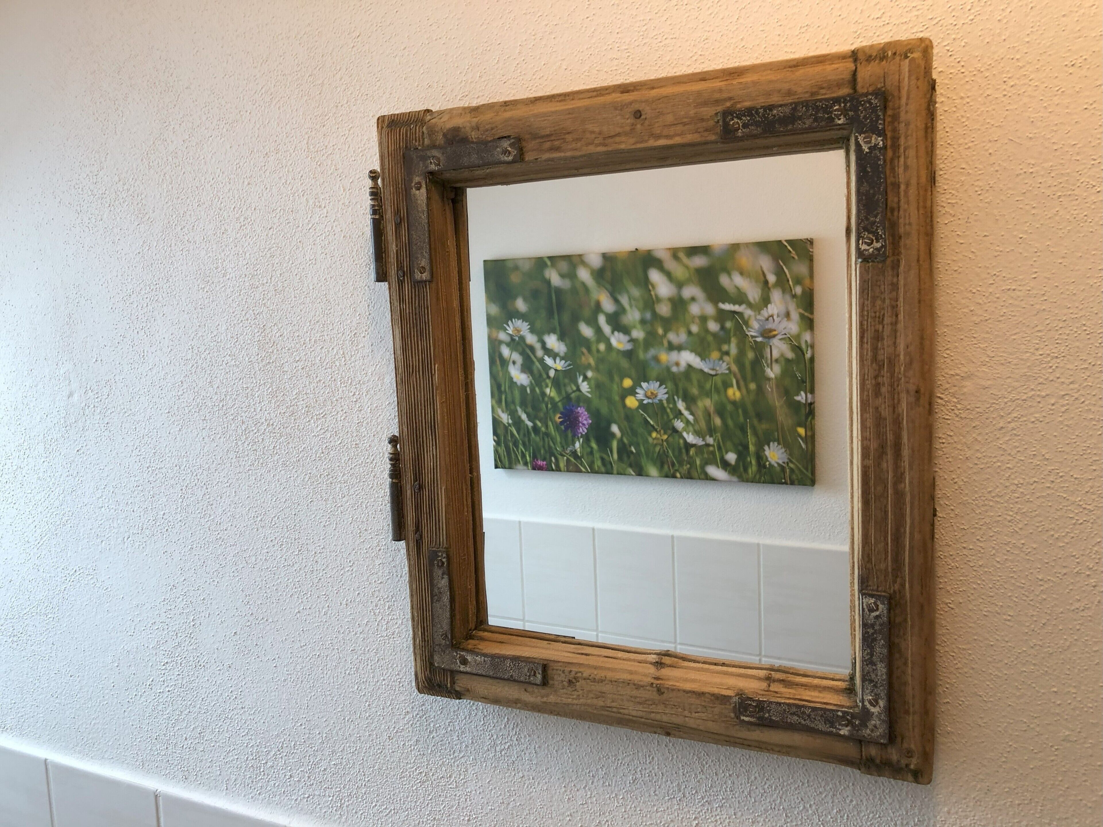 A rustic wooden picture frame with a floral painting on a textured wall.