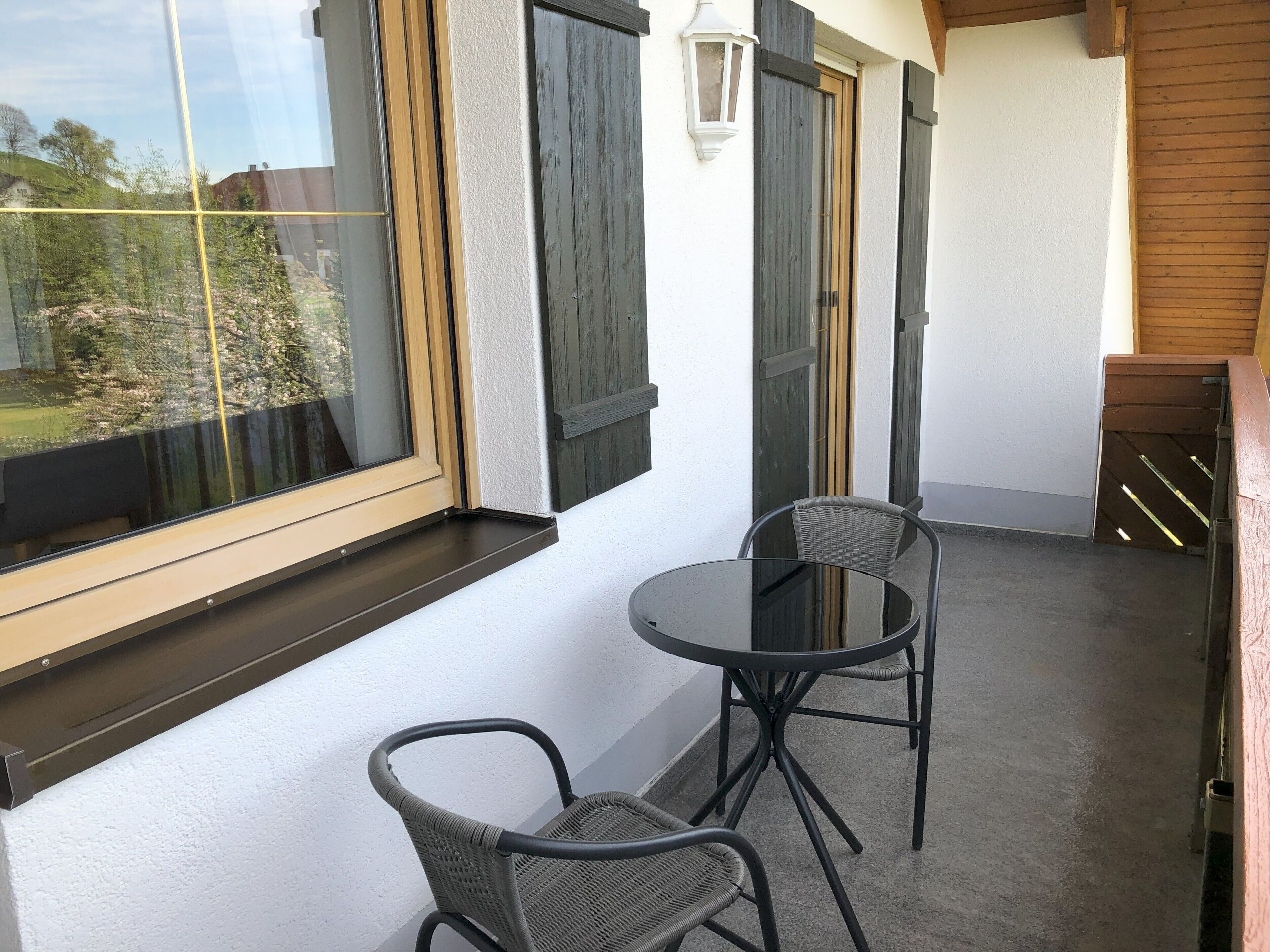 Ein Balkon mit zwei Korbstühlen, einem Glastisch und Blick ins Grüne.