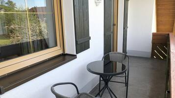 Ein Balkon mit zwei Korbstühlen, einem Glastisch und Blick ins Grüne.