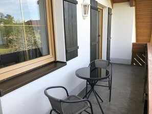 Un balcon avec deux fauteuils en osier, une table en verre et une vue sur la verdure.