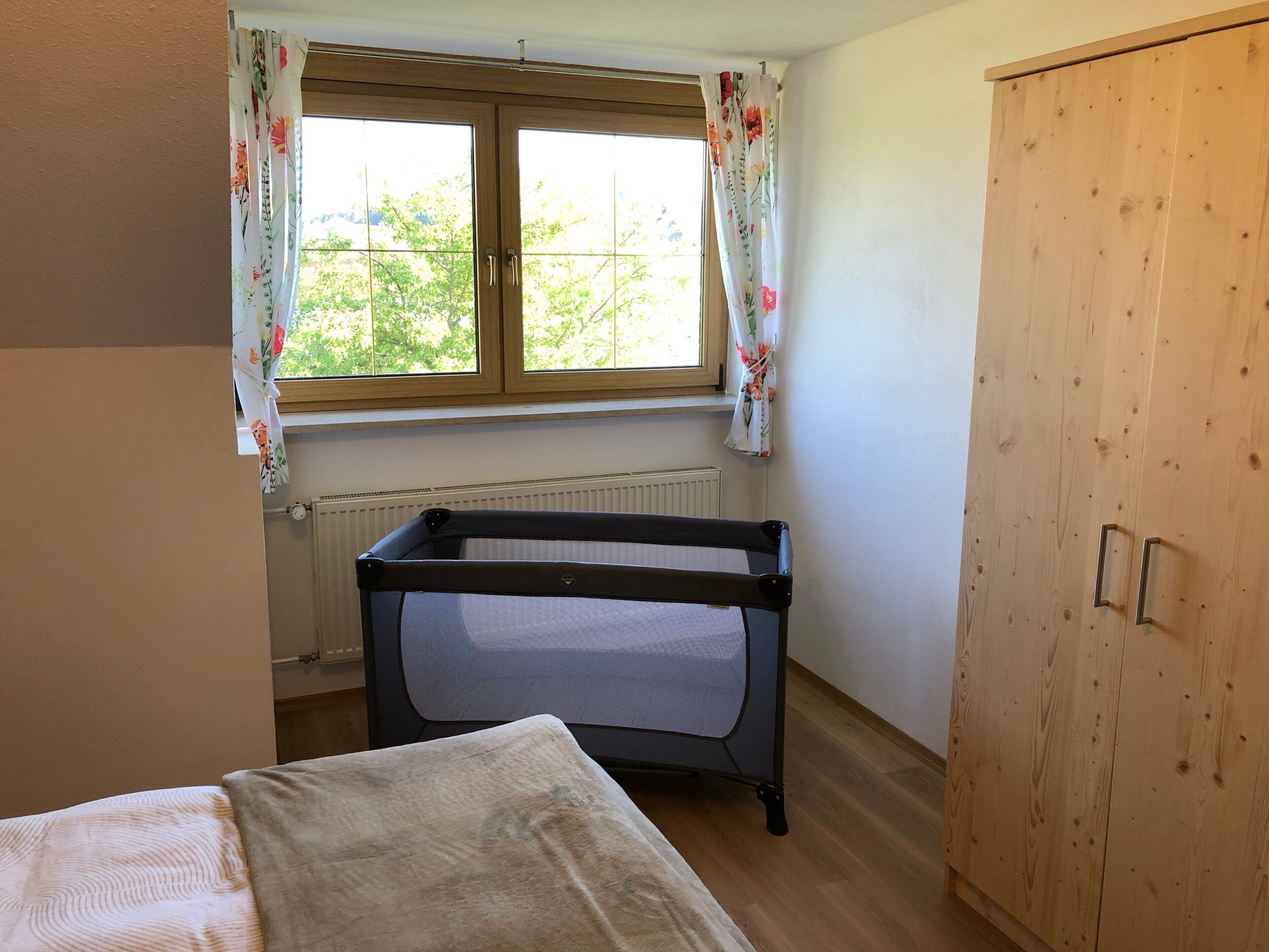 Une pièce avec une fenêtre, un lit, une armoire en bois et un berceau.