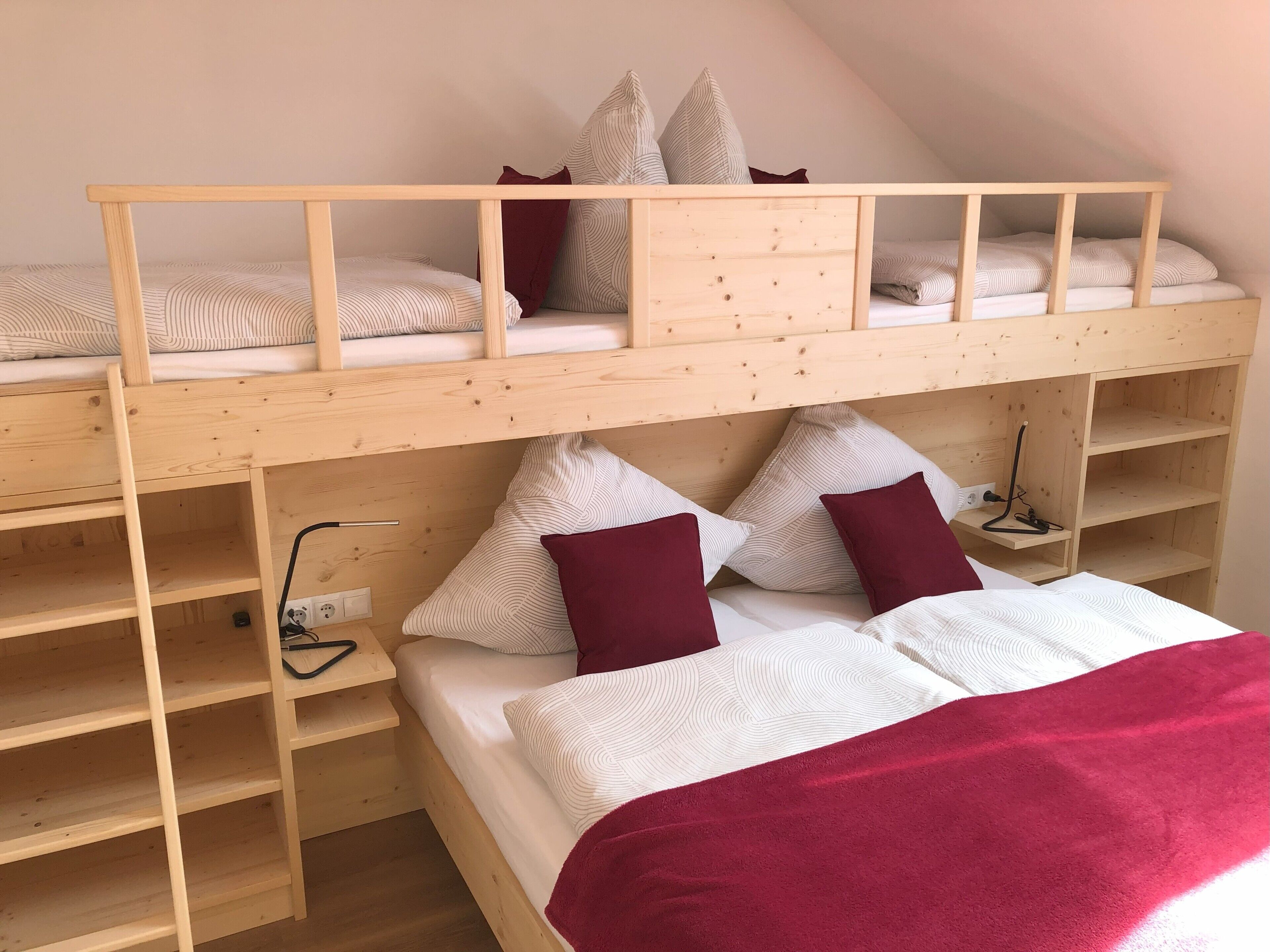 Een stapelbed met houten frame, twee kussens, een deken en een nachtkastje met een lamp.
