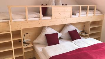 Een stapelbed met houten frame, twee kussens, een deken en een nachtkastje met een lamp.