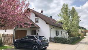 Un immeuble résidentiel avec une allée pavée, une voiture garée et des arbres en fleurs.