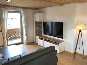 Moderni olohuone, jossa on litteänäyttöinen televisio, puulattia, sohva, pieni pöytä ja lattiavalaisin.
