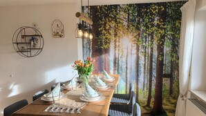 Un coin repas avec une table en bois dressée pour quatre personnes, des chaises, un vase de tulipes et une fresque représentant une forêt sur le mur.