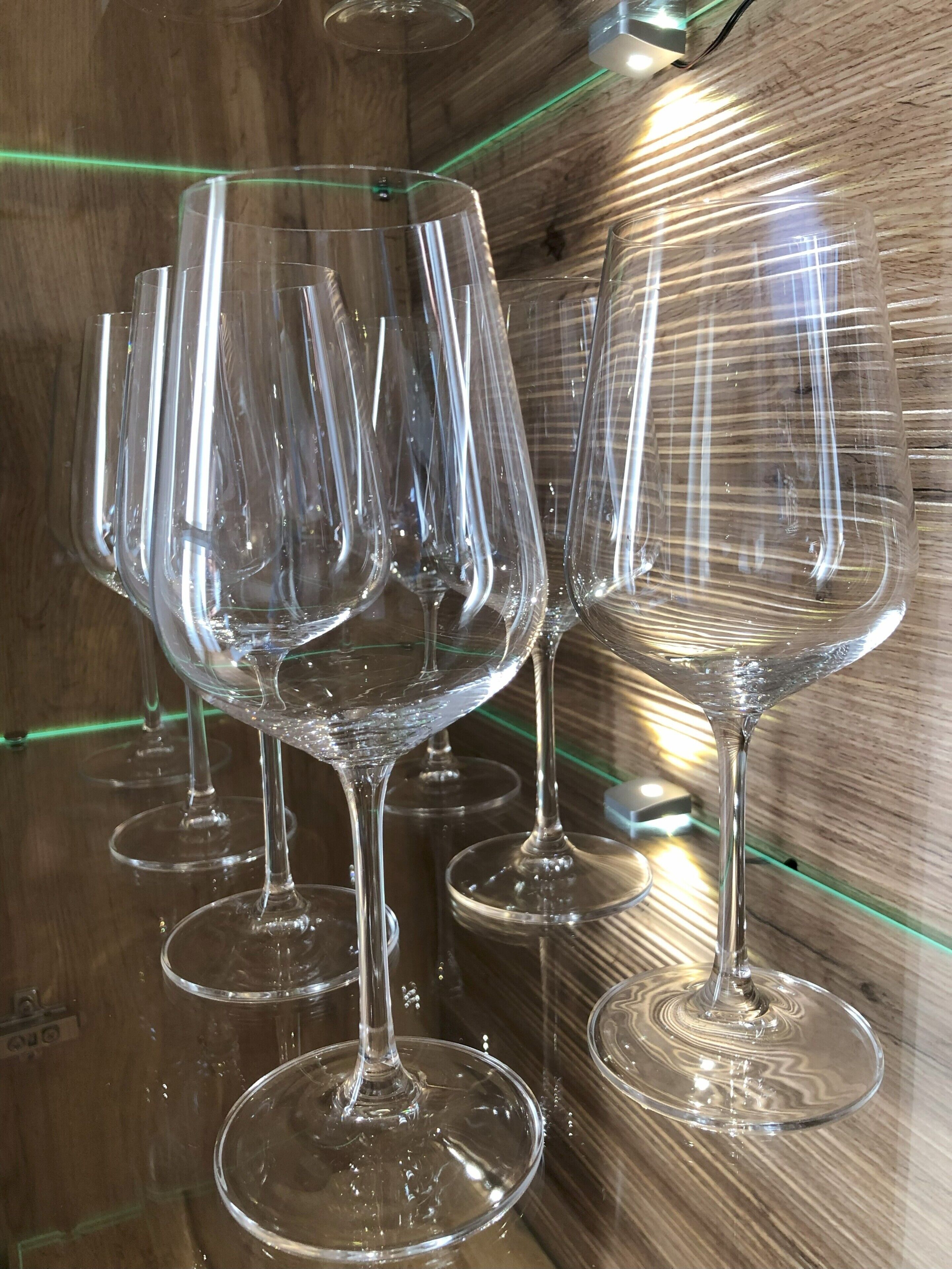 A row of clear wine glasses on a wooden surface with a green light reflection.