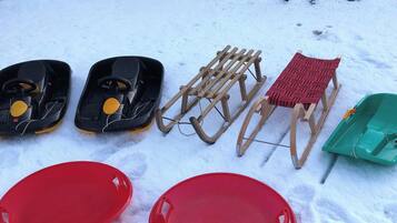 Snowshoes, a sled, and two red sleds on snow.