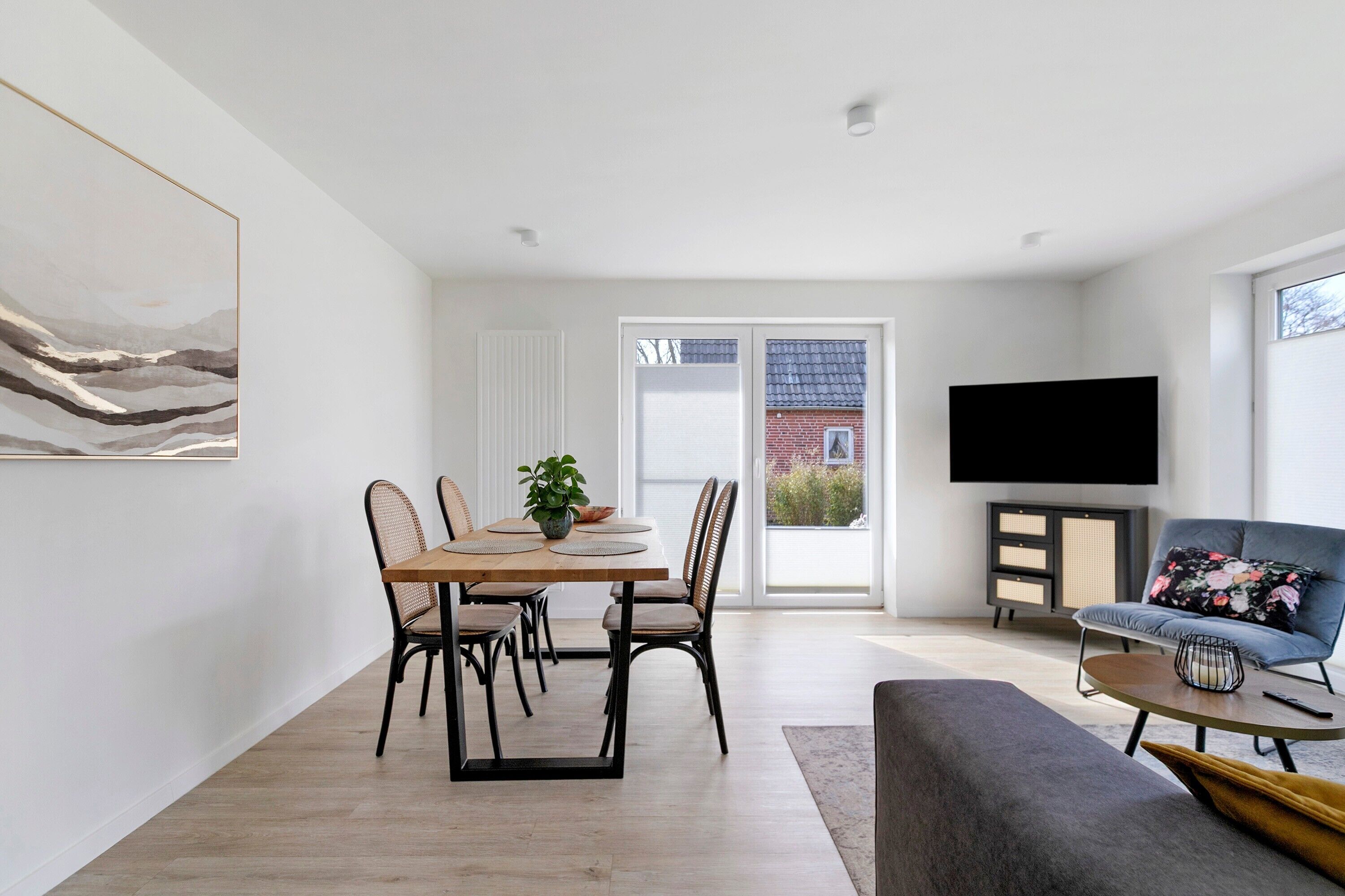 A modern living room with a dining area, a flat-screen TV, and a large window.