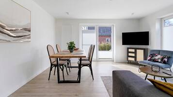 A modern living room with a dining area, a flat-screen TV, and a large window.